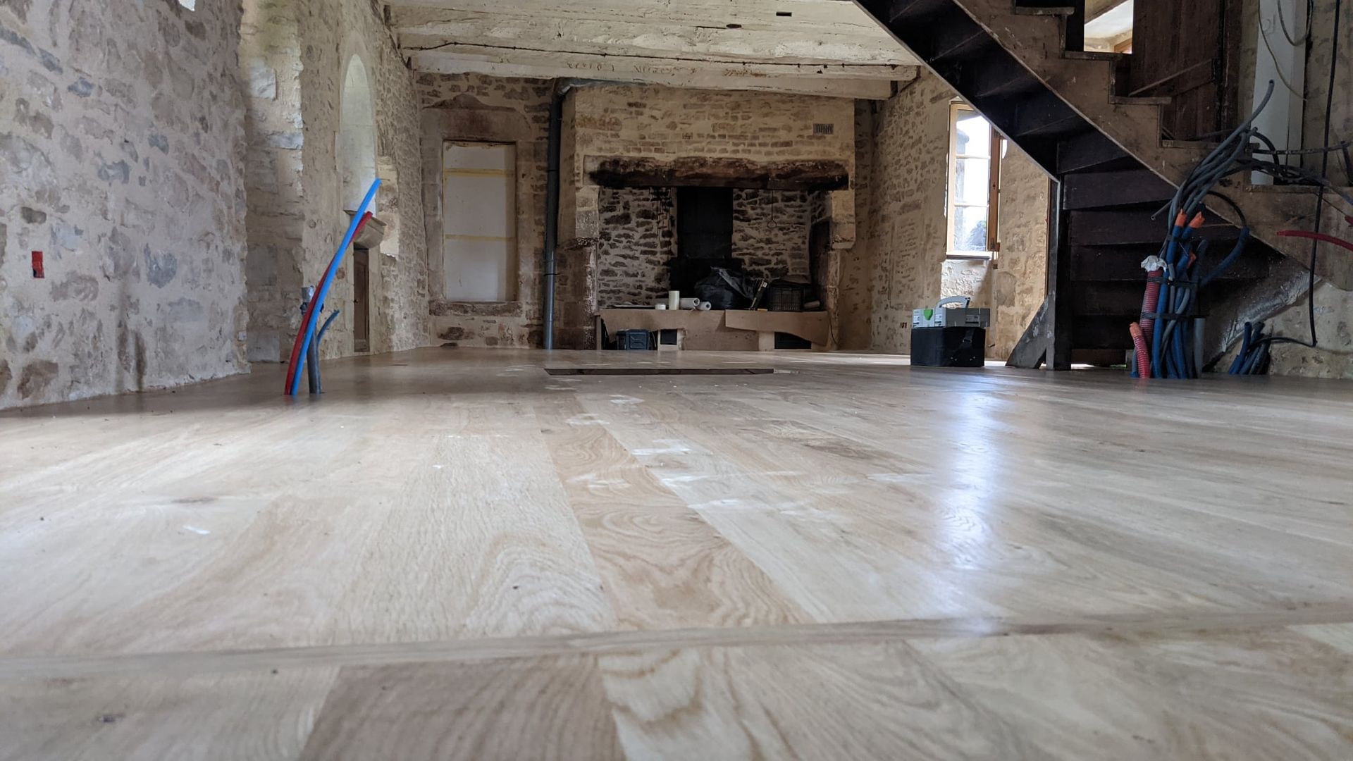 Pièce rustique vide avec parquet, murs en pierre, cheminée et escalier sur la droite