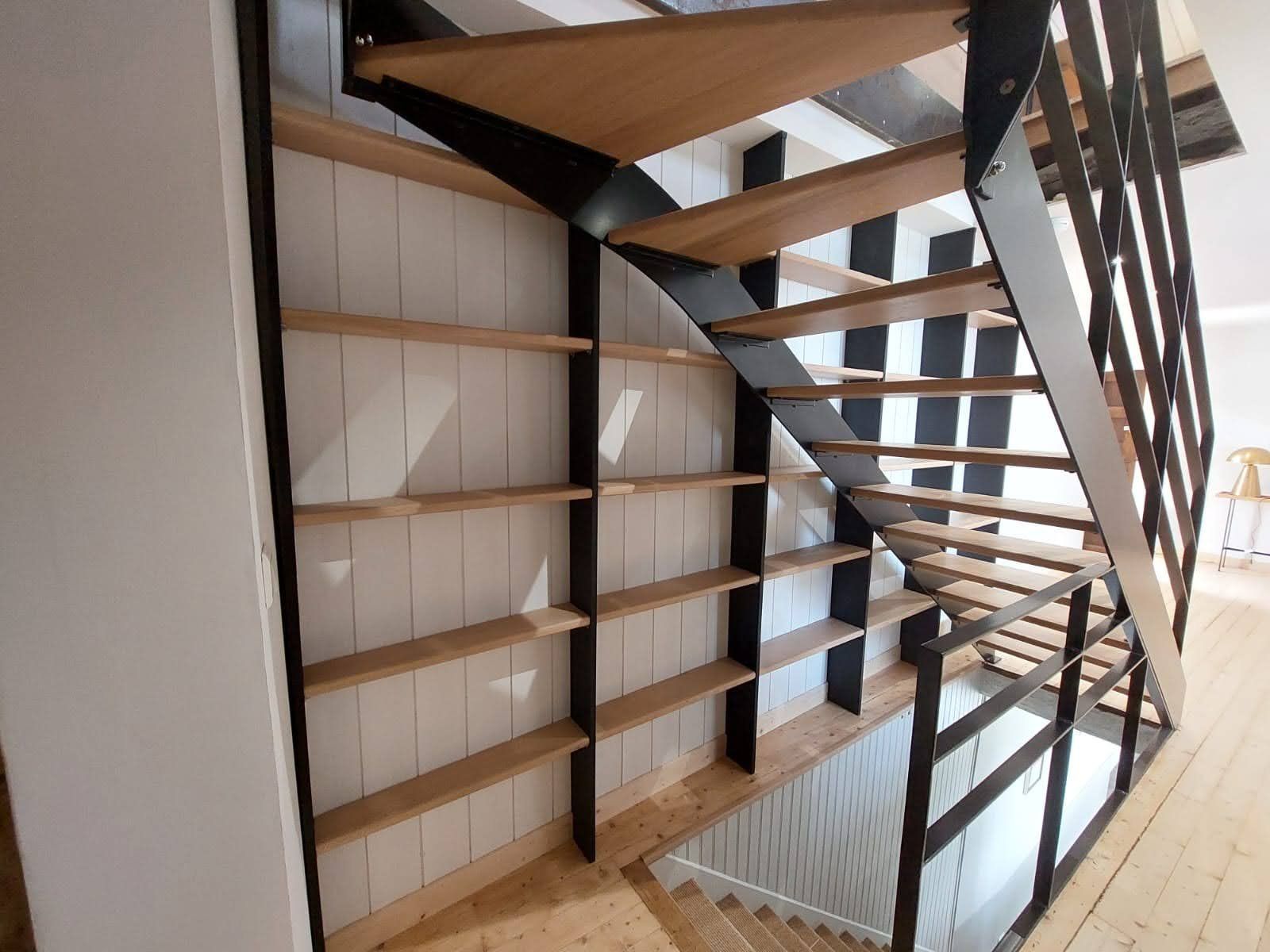 Escalier moderne avec rampes en métal foncé et marches en bois à côté d'étagères murales vides