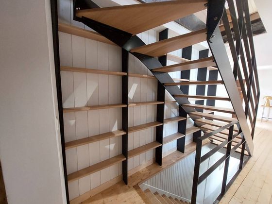 Escalier ouvert avec rampes en métal noir et marches en bois à côté d'étagères intégrées dans un intérieur lumineux