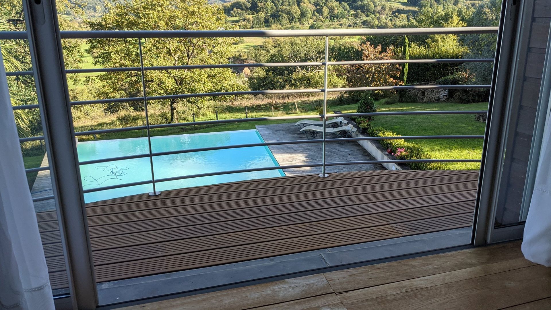 Vue depuis l'intérieur sur une terrasse arrière avec piscine, balustrade et pelouse verdoyante baignée de soleil