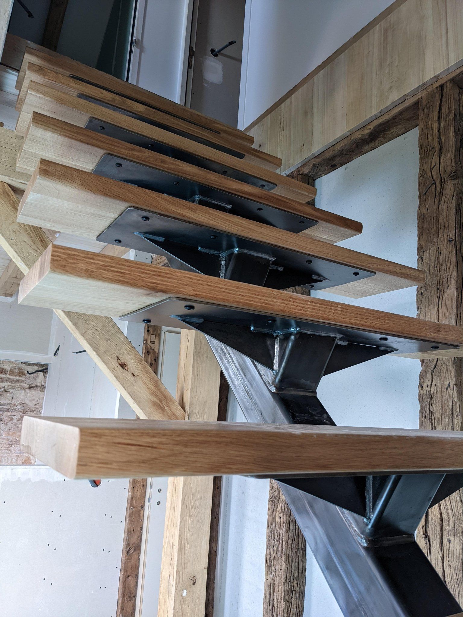 Escalier moderne avec marches en bois et supports en métal noir dans un espace intérieur étroit