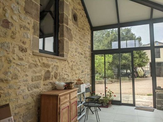 Patio entouré de murs en pierre avec un meuble en bois, une chaise en métal et des portes vitrées donnant sur un jardin extérieur