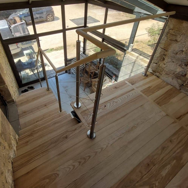 Palier d'escalier en bois avec balustrade en verre donnant sur une terrasse extérieure lumineuse et un espace piscine