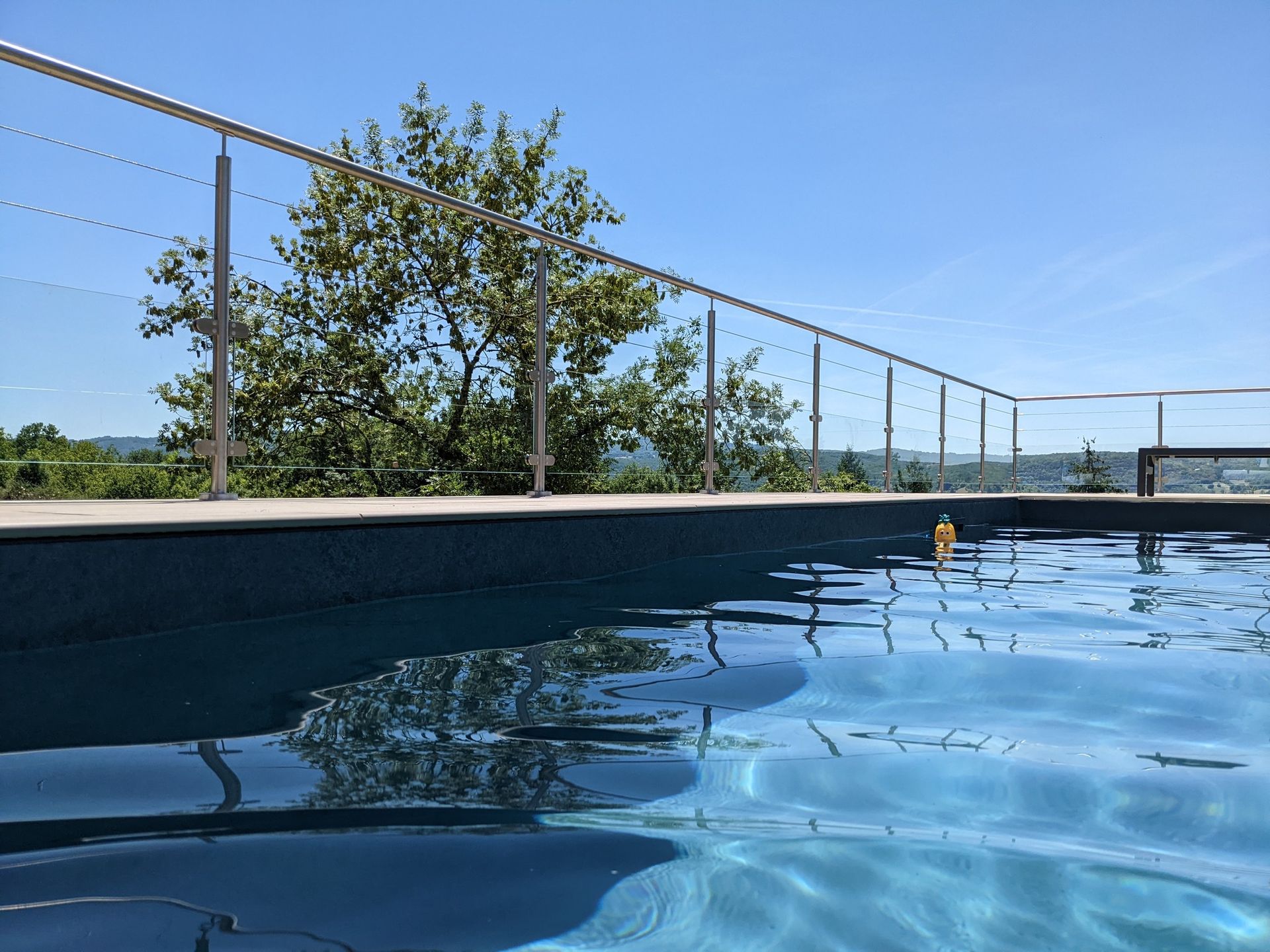 Piscine sur le toit avec eau bleue calme, clôture et arbres sous un ciel dégagé.