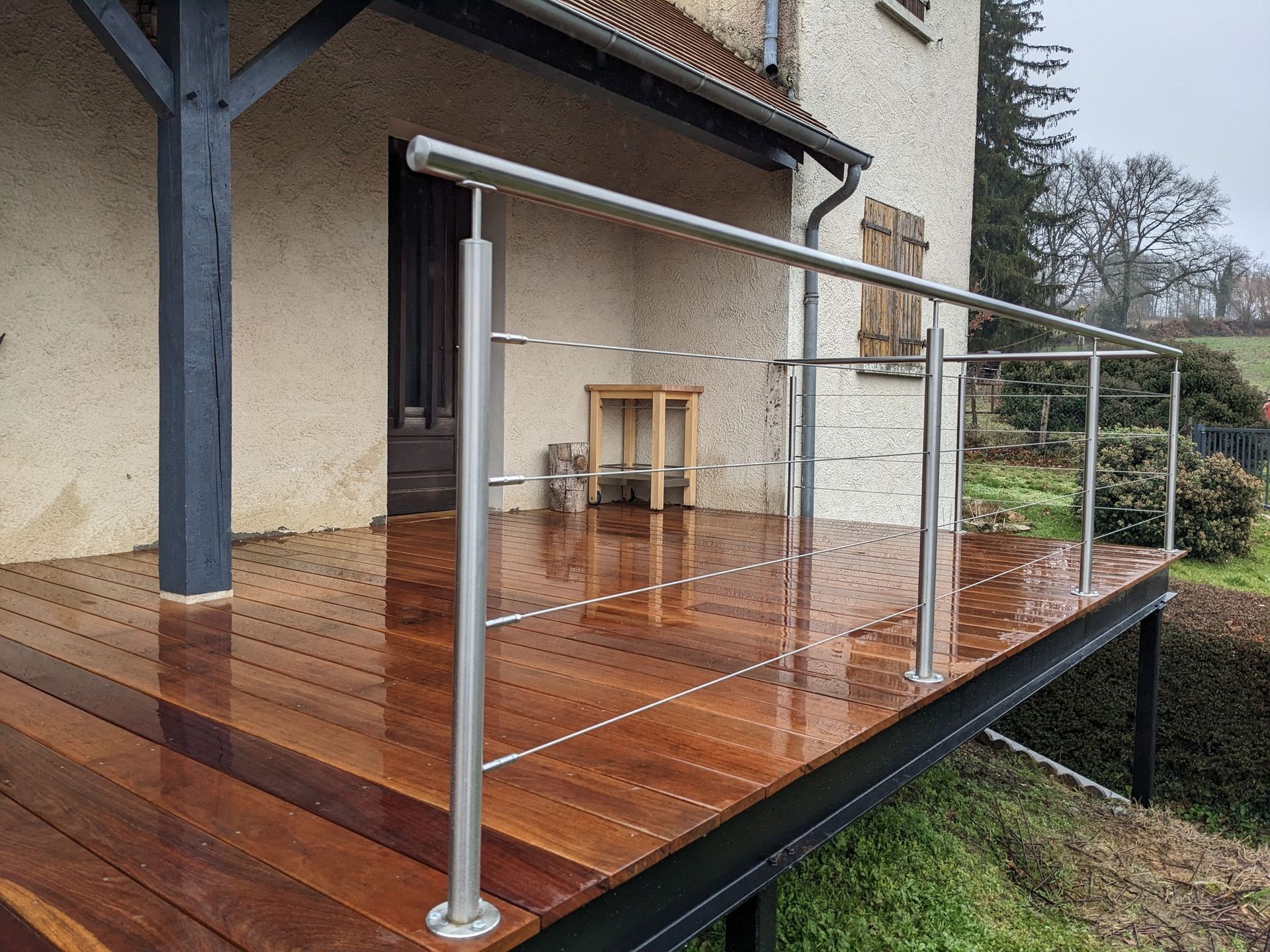 Terrasse en bois avec rambarde en verre jouxtant une maison, donnant sur un versant boisé.