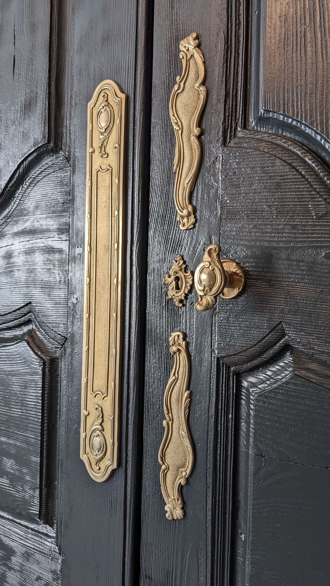 Gros plan sur une porte noire ornée d'une poignée et de moulures dorées, montrant des éclats de peinture et des signes d'usure.
