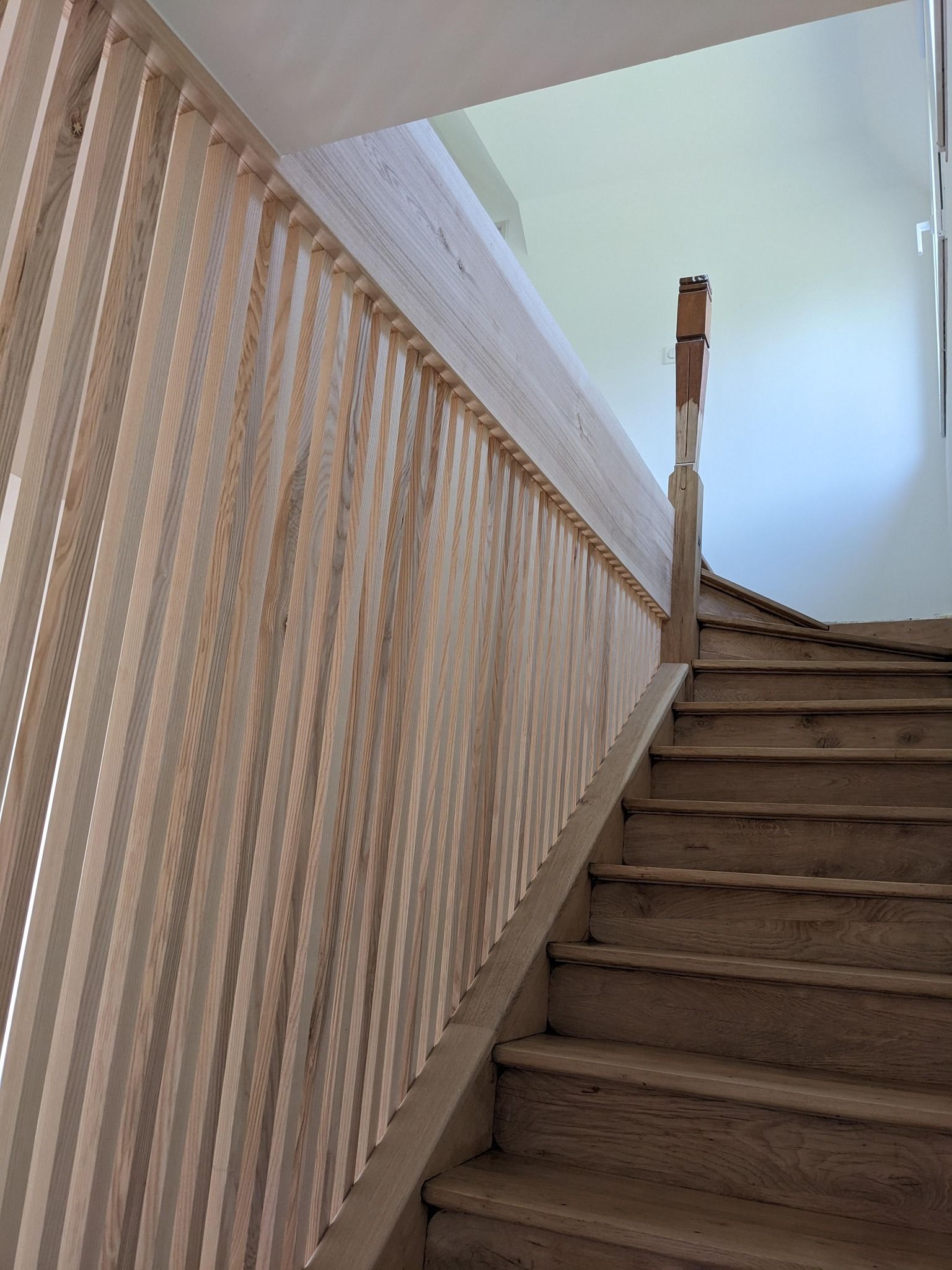 Cage d'escalier avec marches recouvertes de moquette, mur à rayures beiges et puits de lumière au plafond ouvert.
