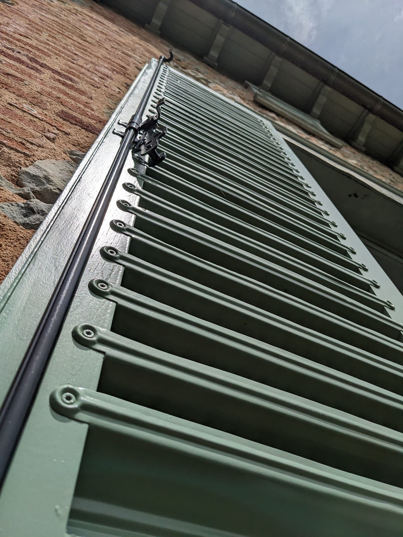 Échelle métallique verte appuyée contre un mur de briques, vue d'en bas.