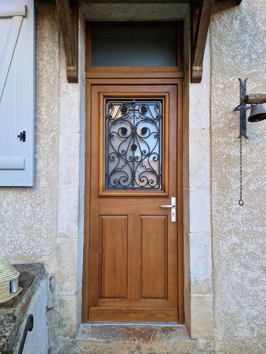 Porte d'entrée en bois avec panneau de verre orné, encastrée dans un mur extérieur en pierre.