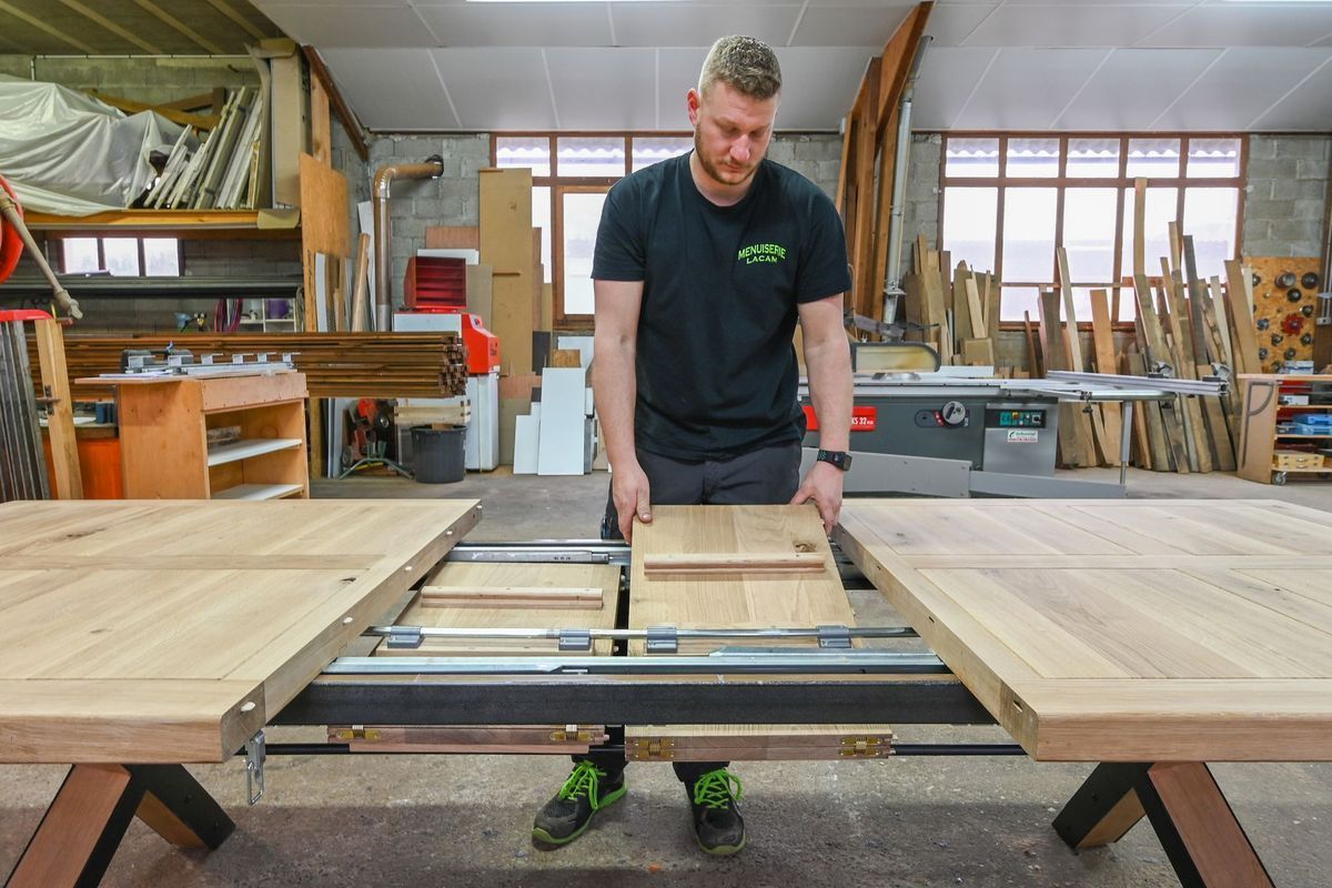 Un homme utilise une scie circulaire pour découper un grand panneau de bois dans un atelier.