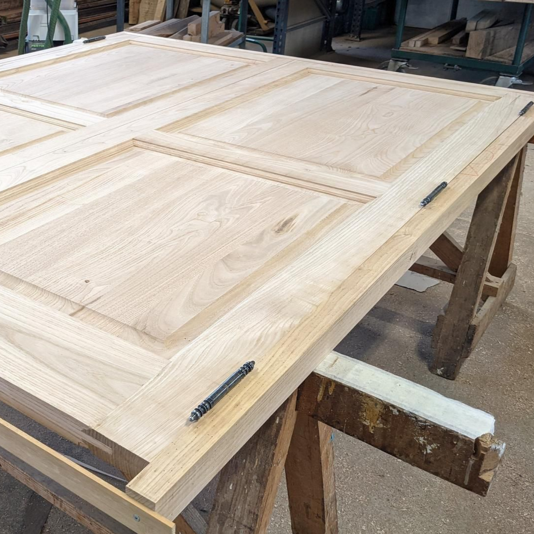 Panneaux de portes d'armoires en bois clair dans un atelier, posés sur un établi avec des serre-joints.