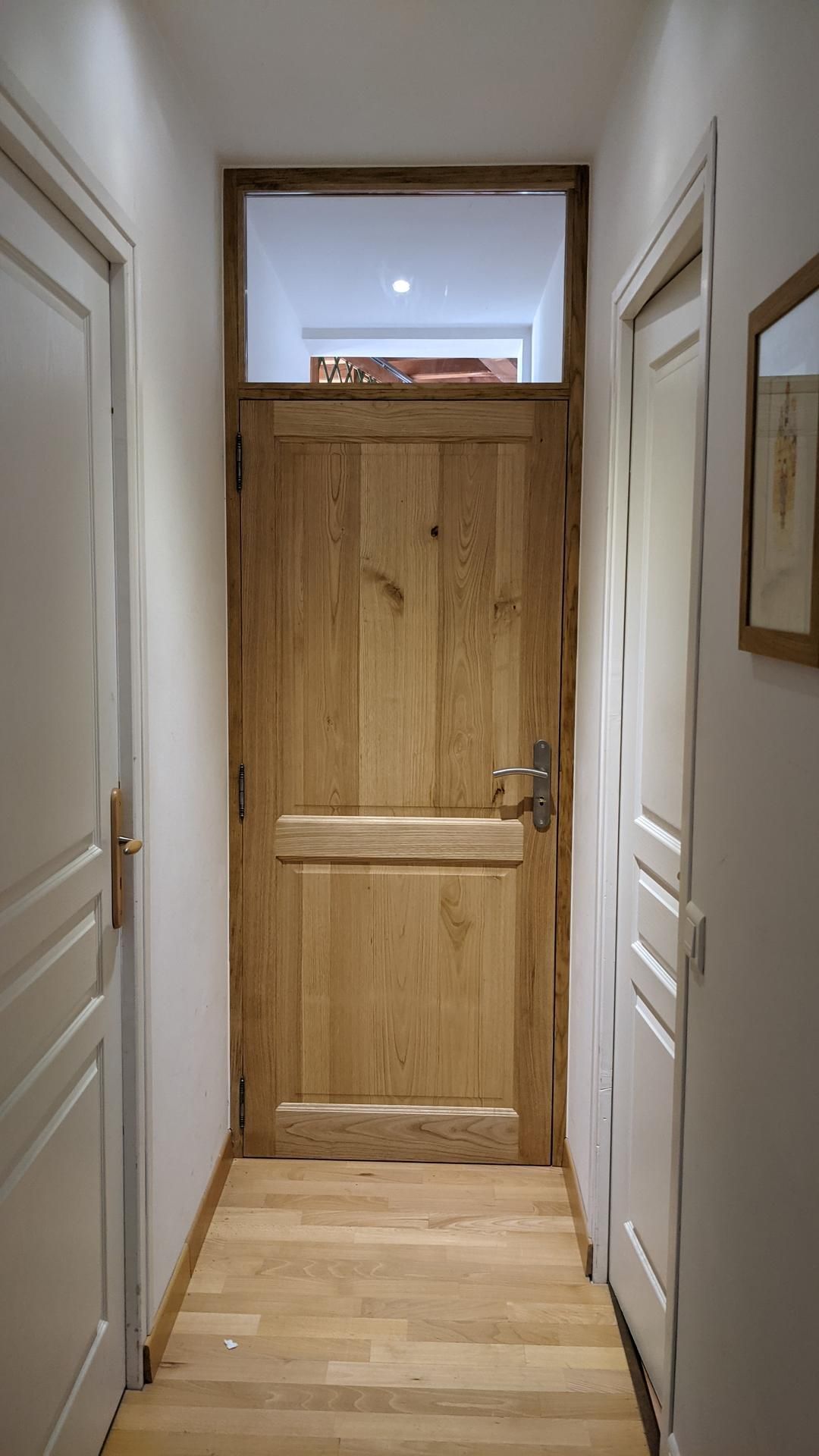 Couloir étroit aux murs blancs et une porte en bois rustique au fond.