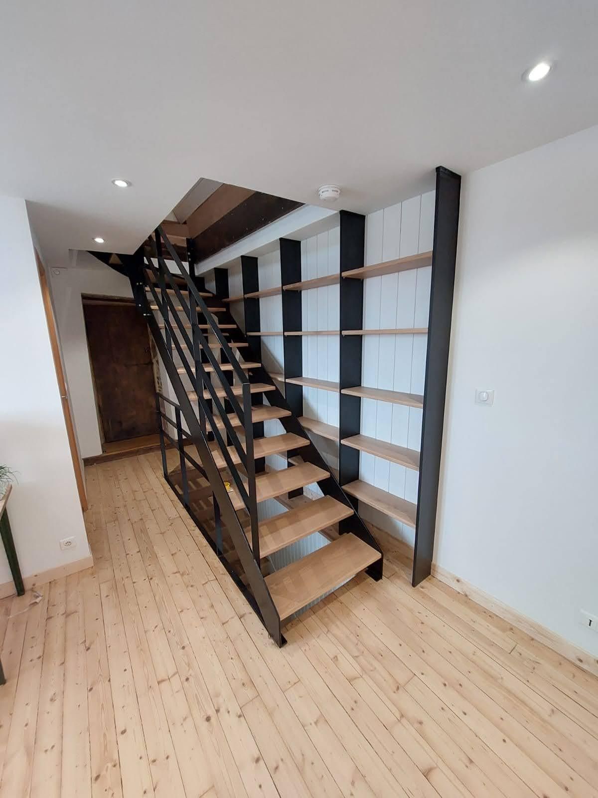 Intérieur moderne avec un escalier en bois, une rampe noire et un parquet clair dans une pièce étroite