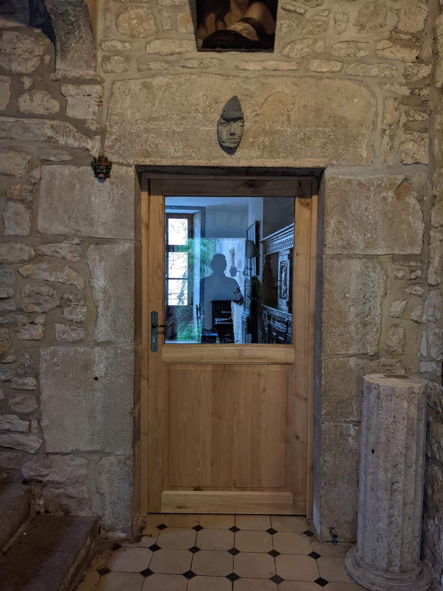 Mur en pierre avec une porte en bois et en verre donnant sur une pièce intérieure lumineuse