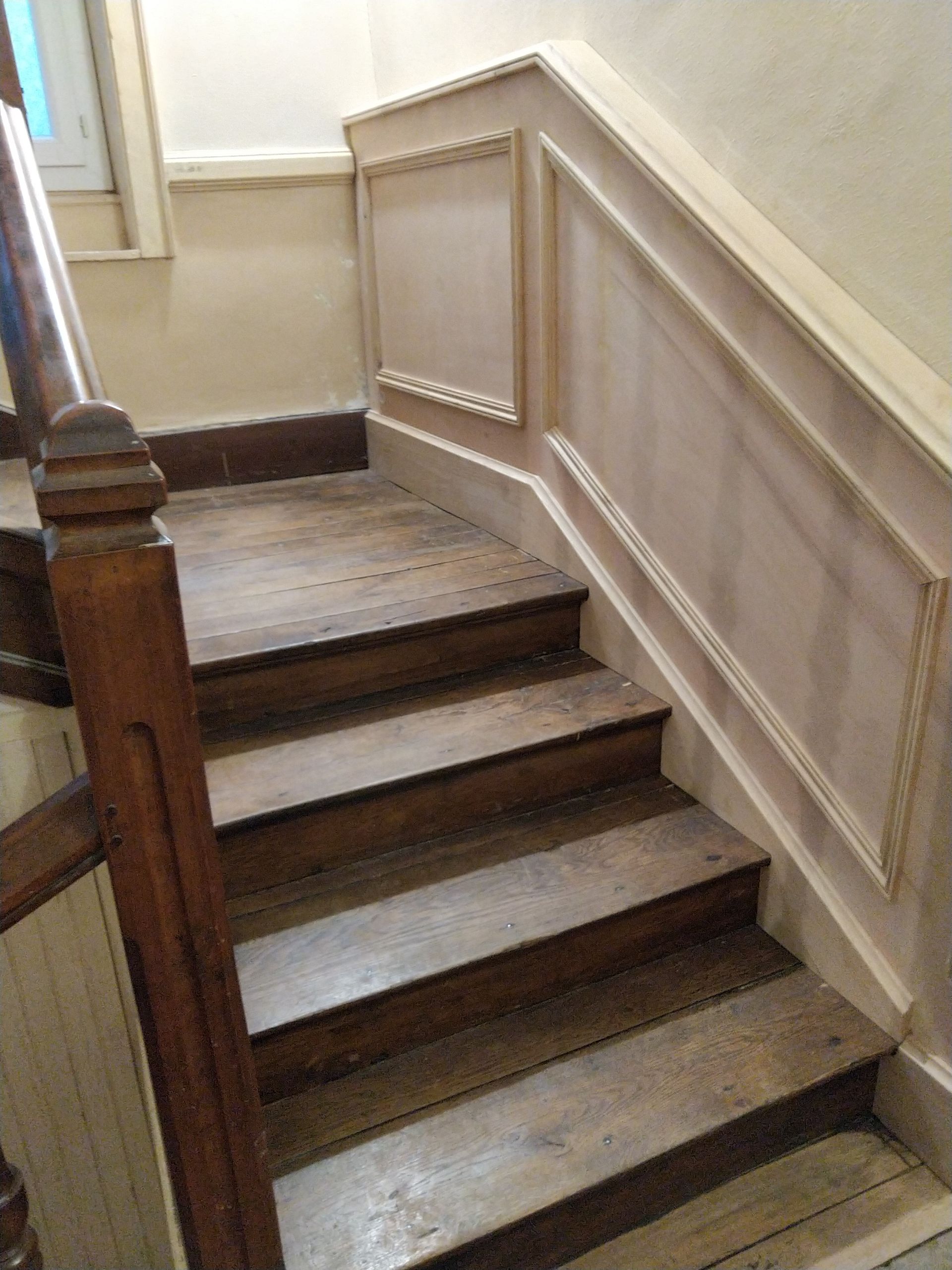 Escalier en bois avec murs et rampe beiges dans un couloir intérieur
