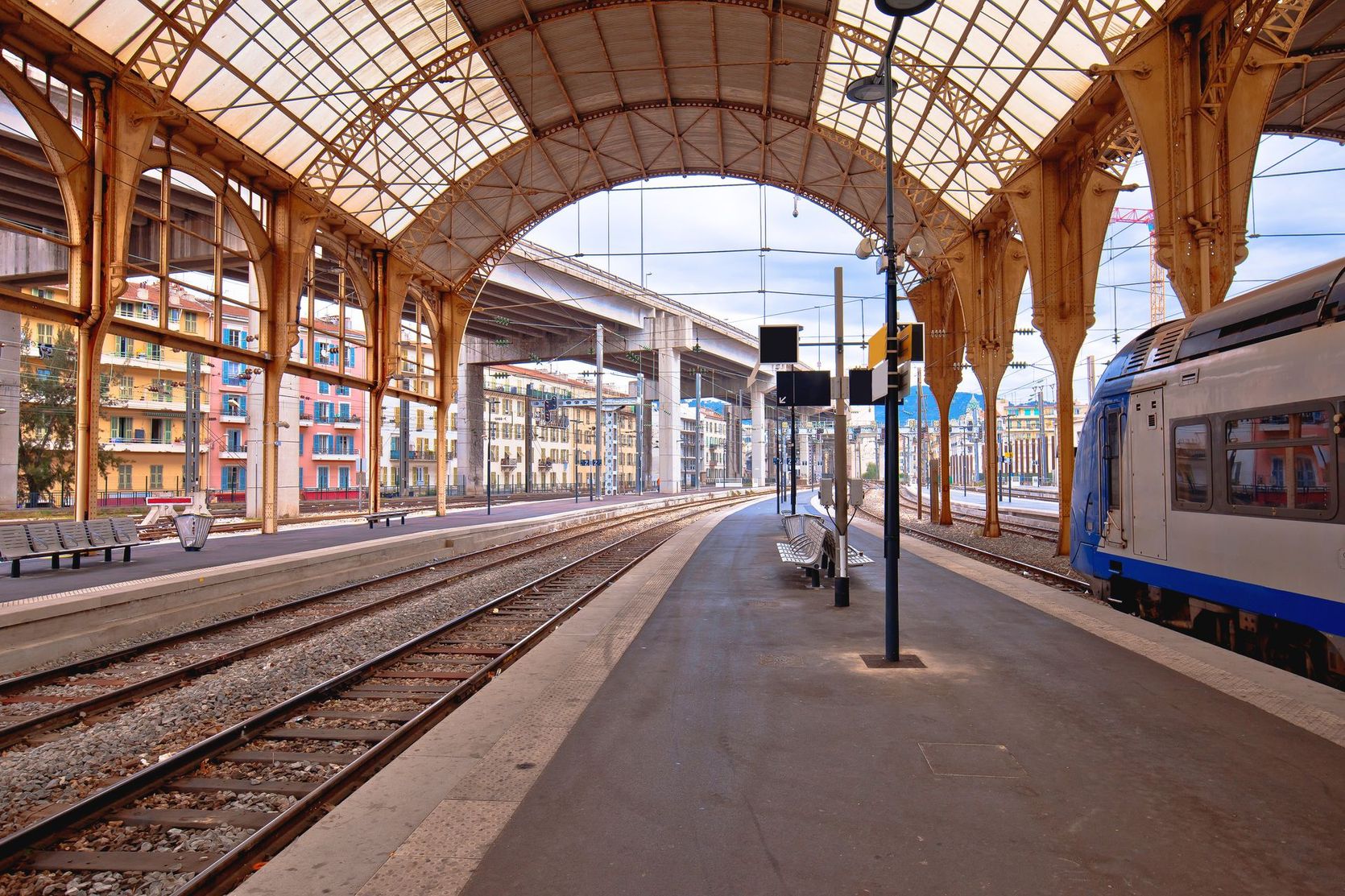 Quai couvert d'une gare avec des voies ferrées et un train bleu et blanc à droite