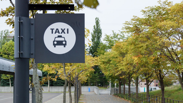 Panneau de taxi sur un poteau au bord d'un trottoir bordé d'arbres et d'une route