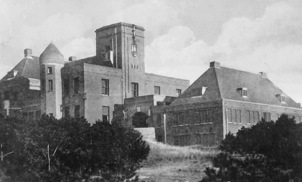 A vintage, black-and-white photograph of a large, multi-story brick building featuring a prominent central clock tower.