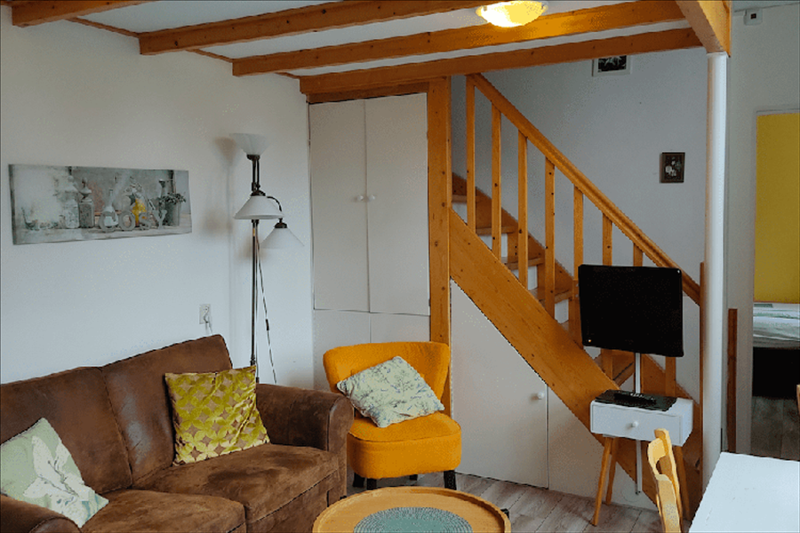 Ein gemütliches Wohnzimmer mit braunem Sofa, gelbem Sessel, Holztreppe und weißen Aufbewahrungsschränken.