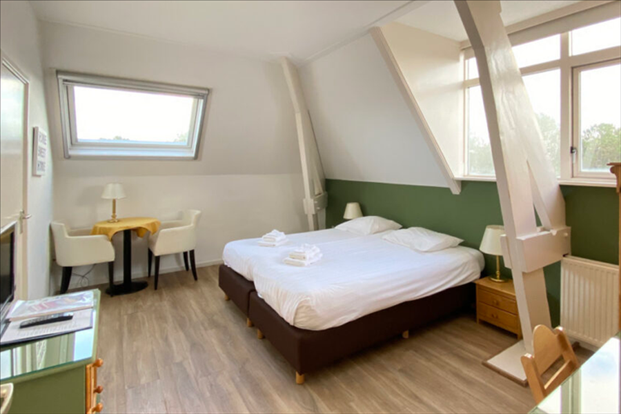 Een hotelkamer op zolder met twee bedden tegen elkaar geschoven, een kleine tafel met stoelen en een lichte houten vloer.