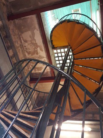 Een laag camerastandpunt van een gele wenteltrap met een donkere metalen leuning in een industrieel gebouw.