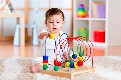 Un bebé está sentado en el suelo jugando con un juguete de madera.