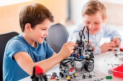 Dos niños pequeños están sentados en una mesa construyendo un robot.