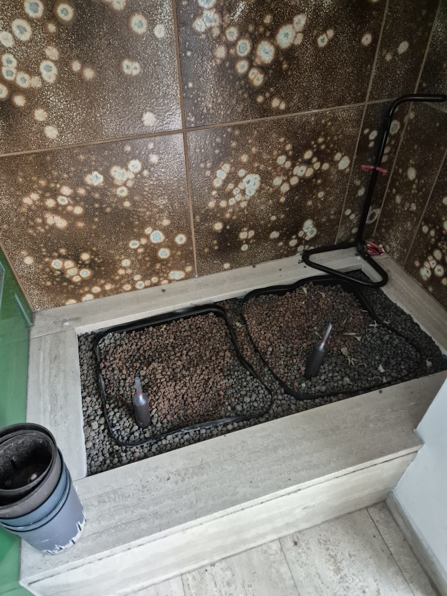 Zwei dunkle Netze liegen in einer hellgrauen Stufenkonstruktion. Der geflieste Hintergrund weist braune Flecken auf. Eine zusammengerollte Matte und ein Draht sind zu sehen.