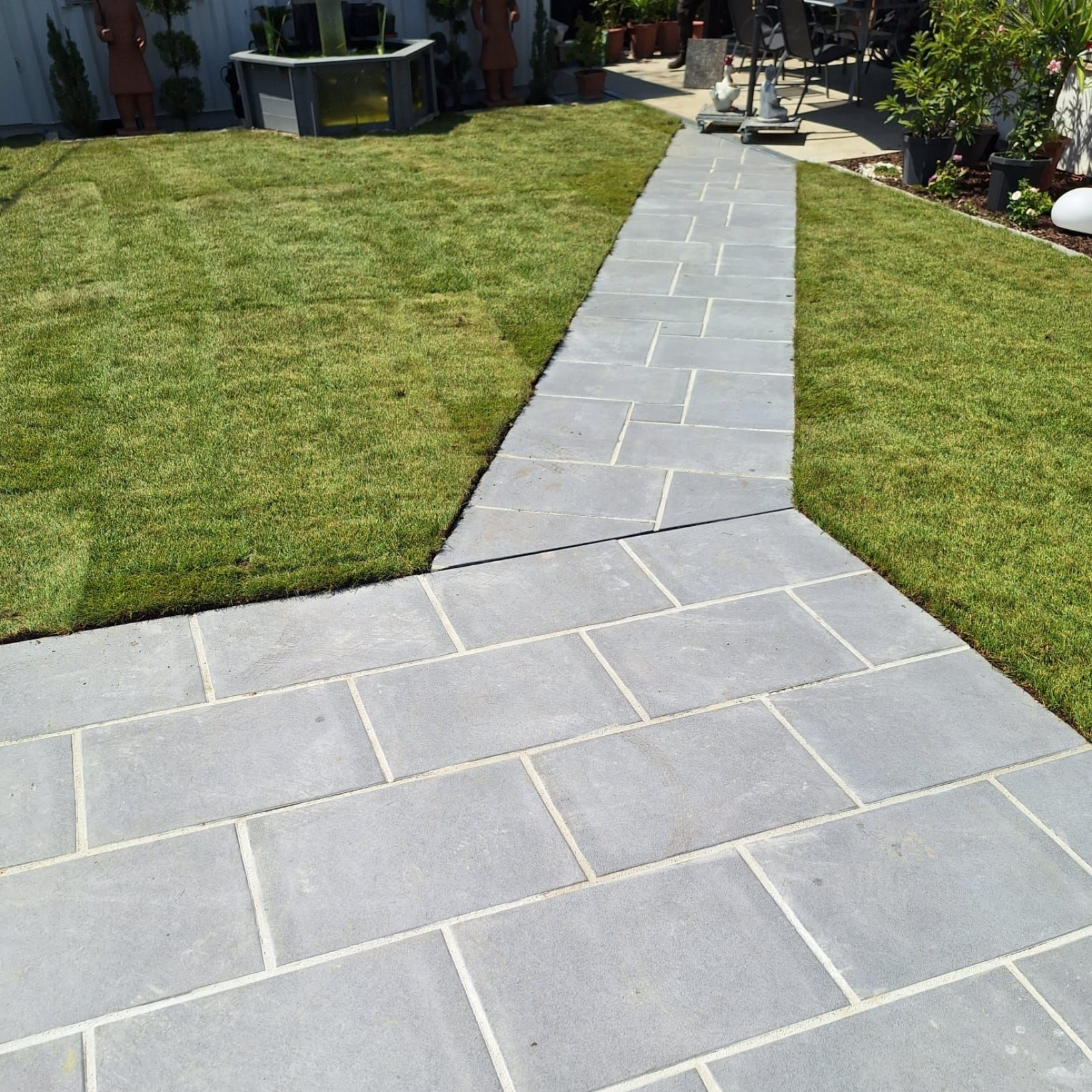 Grauer Steinweg durch einen grünen Rasen in einem Hinterhof.