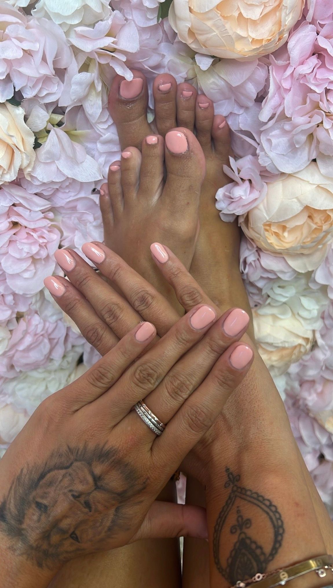 Hände und Füsse mit rosa Nagellack, ruhend auf einem Hintergrund aus hellrosa und weissen Blüten.
