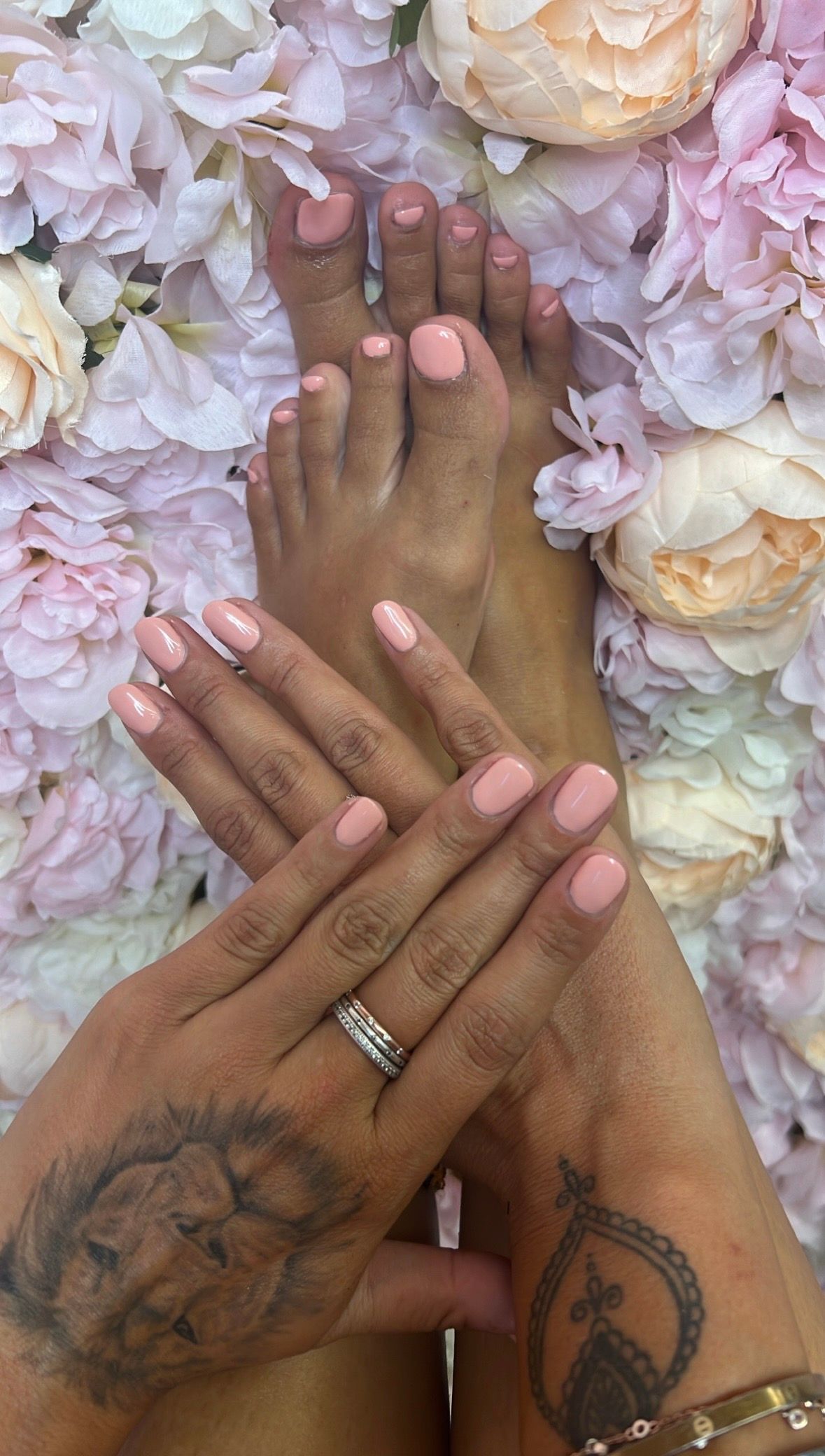 Hände und Füsse mit rosa Nagellack, ruhend auf einem Hintergrund aus hellrosa und weissen Blüten.