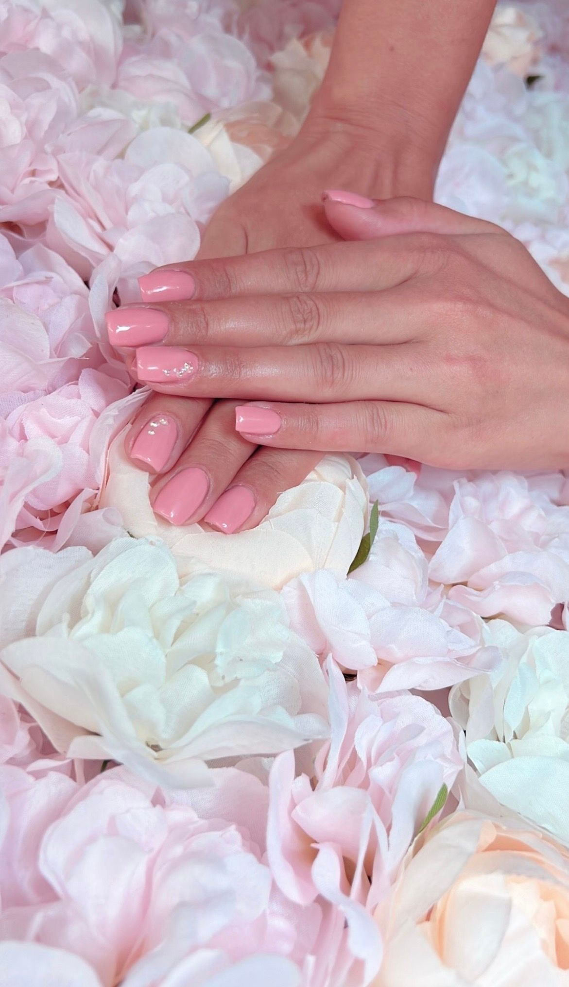 Hände mit rosa Nagellack ruhen auf weissen und rosa Blüten.