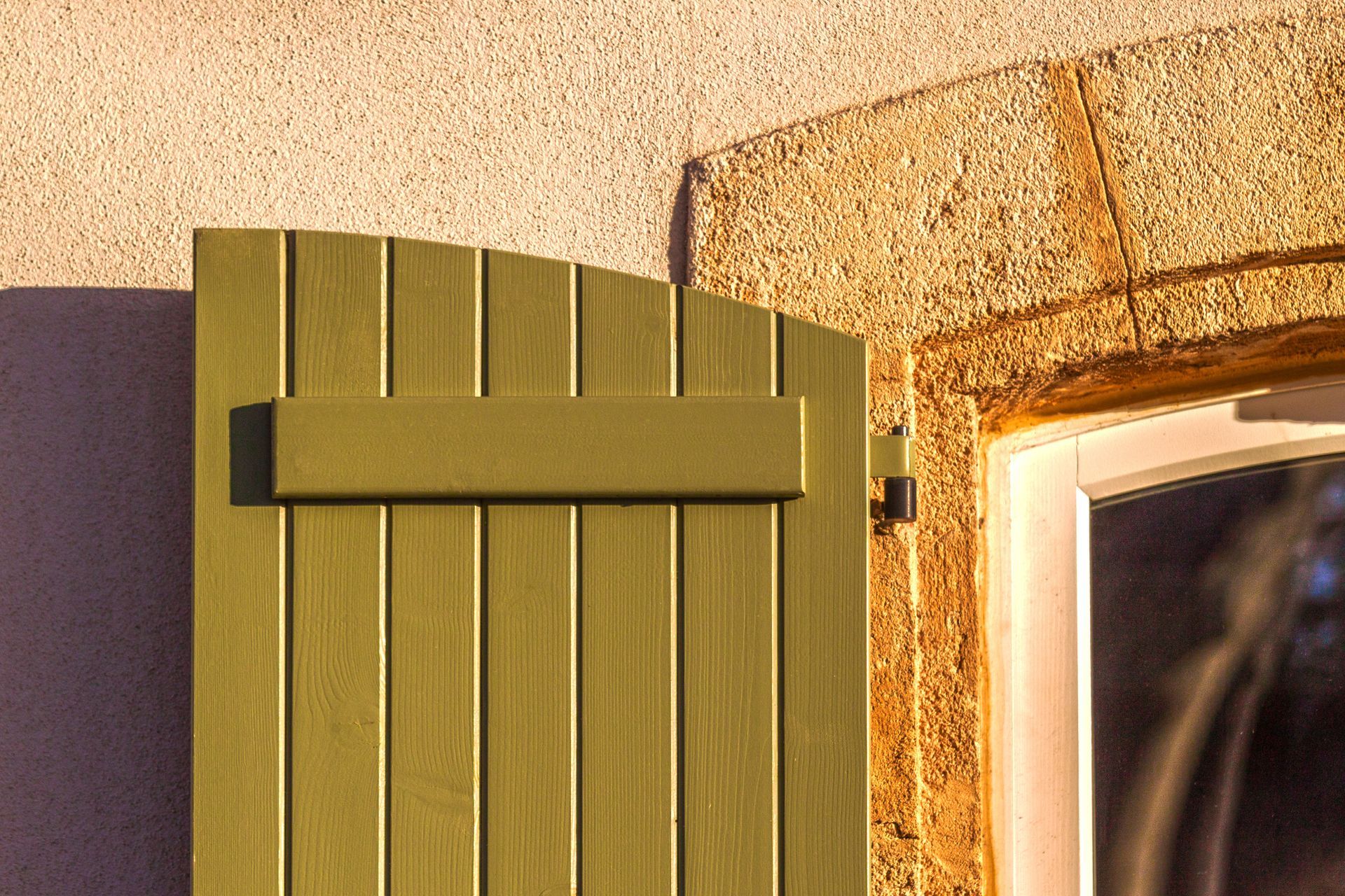 Un volet battant en bois, couleur vert olive.