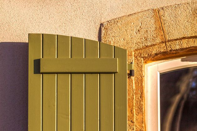 Un volet battant en bois, couleur vert olive.
