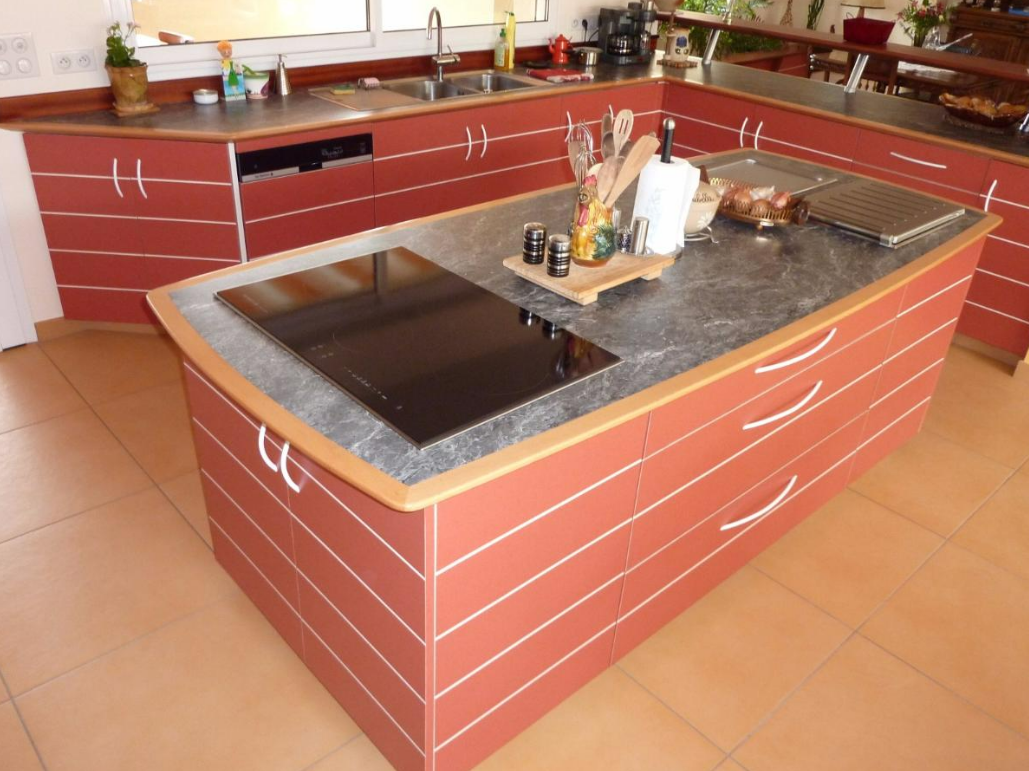 Cuisine moderne avec des meubles rouges et un îlot central équipé d’une plaque de cuisson.
