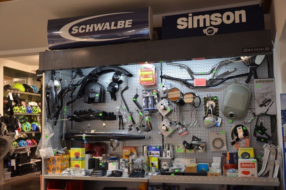 Fahrradteile-Auslage mit Schwalbe- und Simson-Logos, auf der Werkzeuge, Zubehör und verpackte Artikel an einer Ladenwand gezeigt werden.