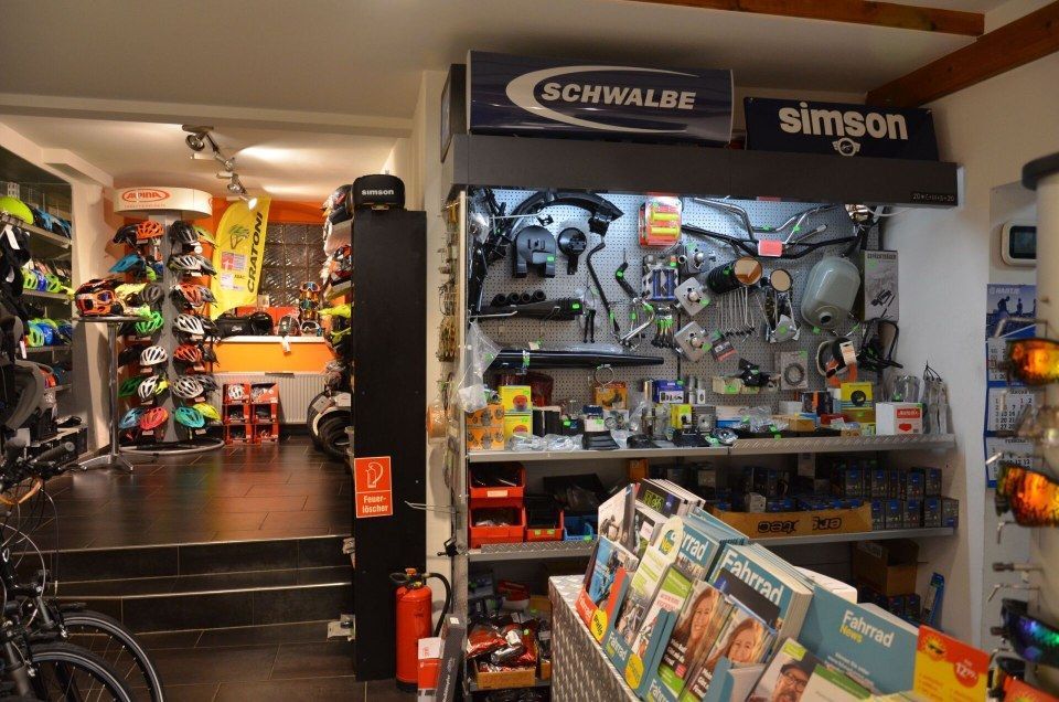Schaufenster eines Fahrradladens mit Schwabe- und Simson-Schildern, Regalen mit Ersatzteilen und einem Ständer mit Broschüren und Werkzeugen