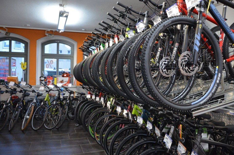 Reihenweise aufgestellte Fahrräder in einem Fahrradladen, viele hängen an Deckenregalen und andere stehen aufgereiht auf dem Boden.