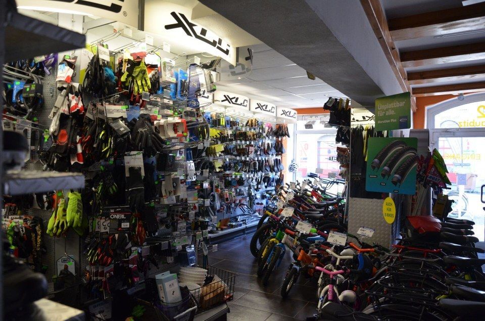 Schaufenster eines Fahrradladens in einem Innenraum mit Helmen, Fahrradteilen und farbenfroher Ausrüstung auf Regalen und Wänden.