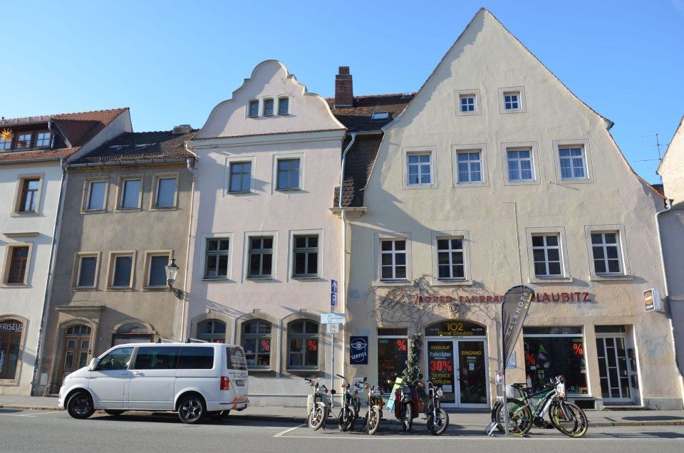 Eine Reihe heller europäischer Stadthäuser mit geparktem Lieferwagen und Fahrrädern an einer sonnigen Straße