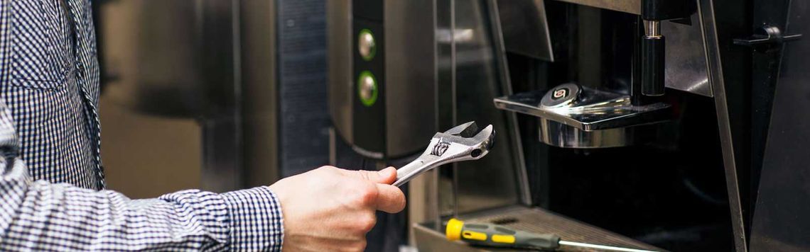 Un hombre está arreglando una máquina de café con una llave inglesa.