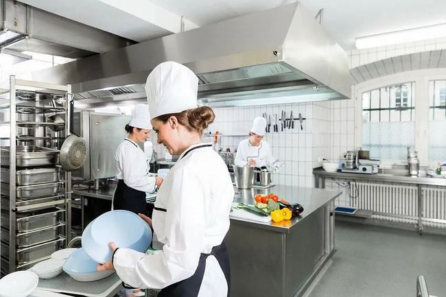 Una mujer con un gorro de chef sostiene un bol en una cocina.