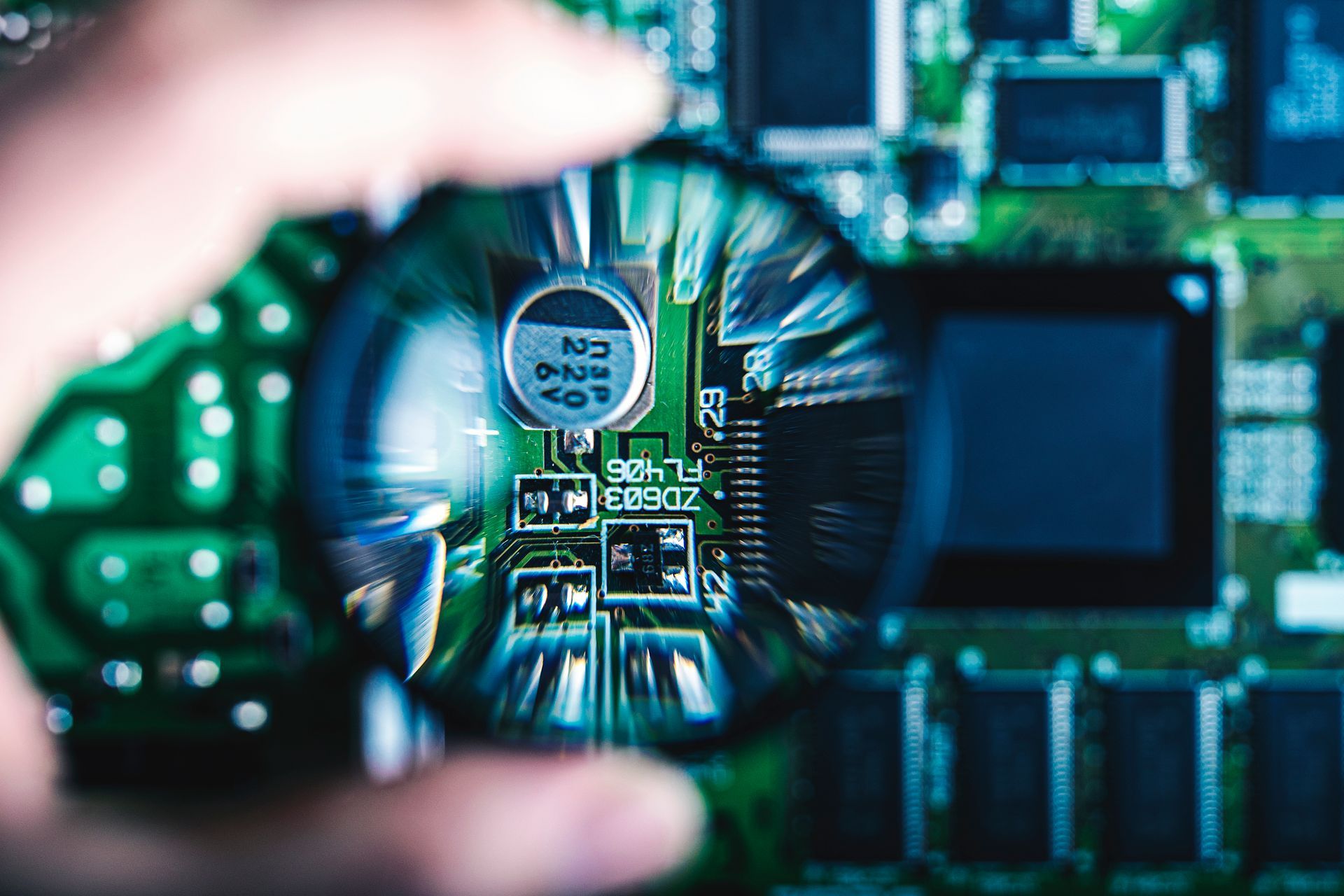 Une main tenant une loupe au-dessus d'un circuit imprimé