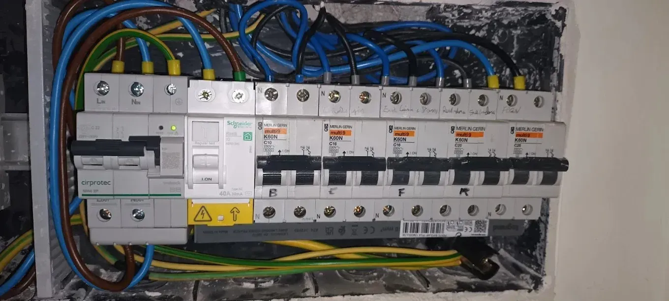 Una unidad de consumo eléctrico abierta con disyuntores, cableado y un interruptor principal montado en una pared.