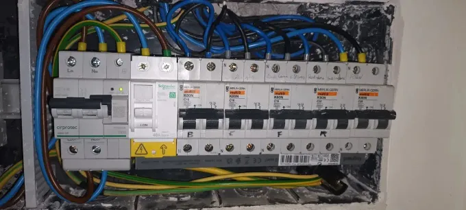 Una unidad de consumo eléctrico abierta con disyuntores, cableado y un interruptor principal montado en una pared.