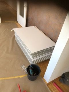 Ein Stapel weißer Fliesen liegt neben einem Eimer auf dem Boden.