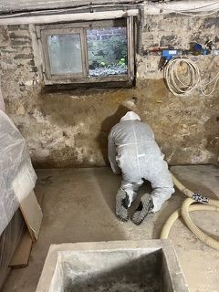 Ein Mann kniet in einem Keller neben einem Fenster auf dem Boden.