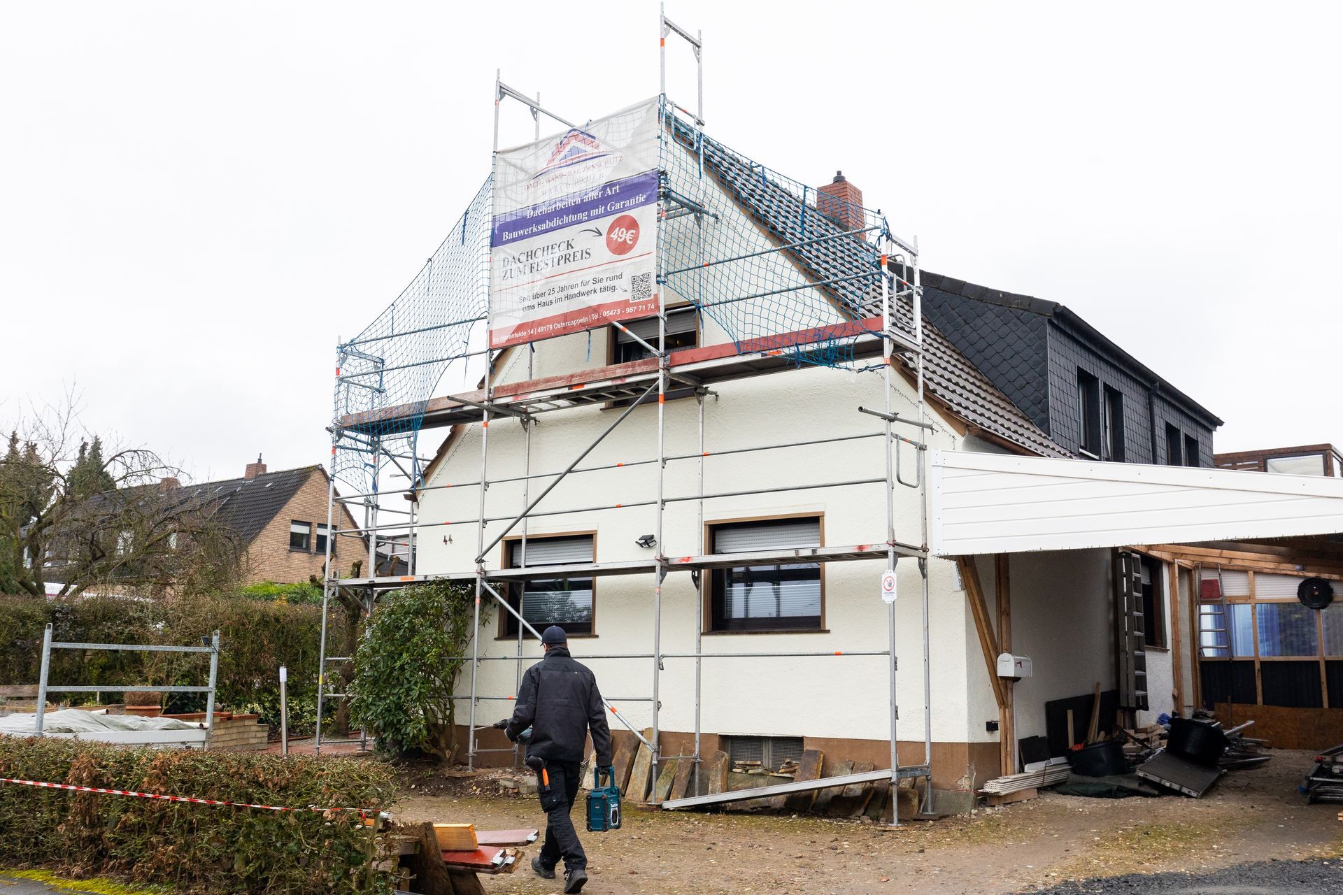 Ein Mann geht vor einem Haus mit einem Gerüst entlang.
