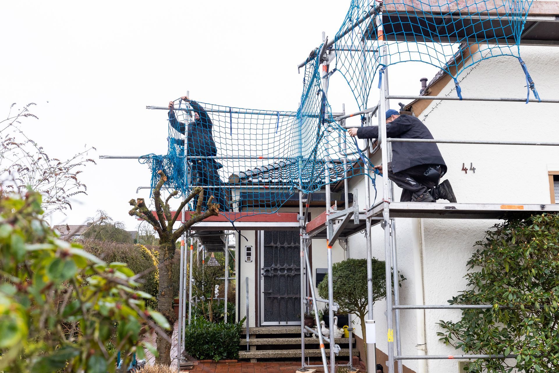 Ein Mann kniet auf einem Gerüst vor einem Haus.