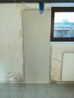 Eine weiße Wand mit einem Fenster und einem Heizkörper in einem Zimmer.